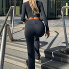Frau in schwarzem Sportanzug geht Treppe hinauf, modernes Fitness-Outfit, urbaner Hintergrund, aktive Mode, bequeme Sportbekleidung.