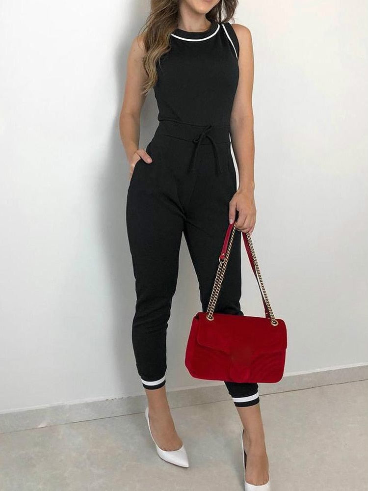 Damen Jumpsuit in Schwarz mit weißen Akzenten, kombiniert mit roter Handtasche und weißen Pumps. Elegante Mode, stilvoll und modern.