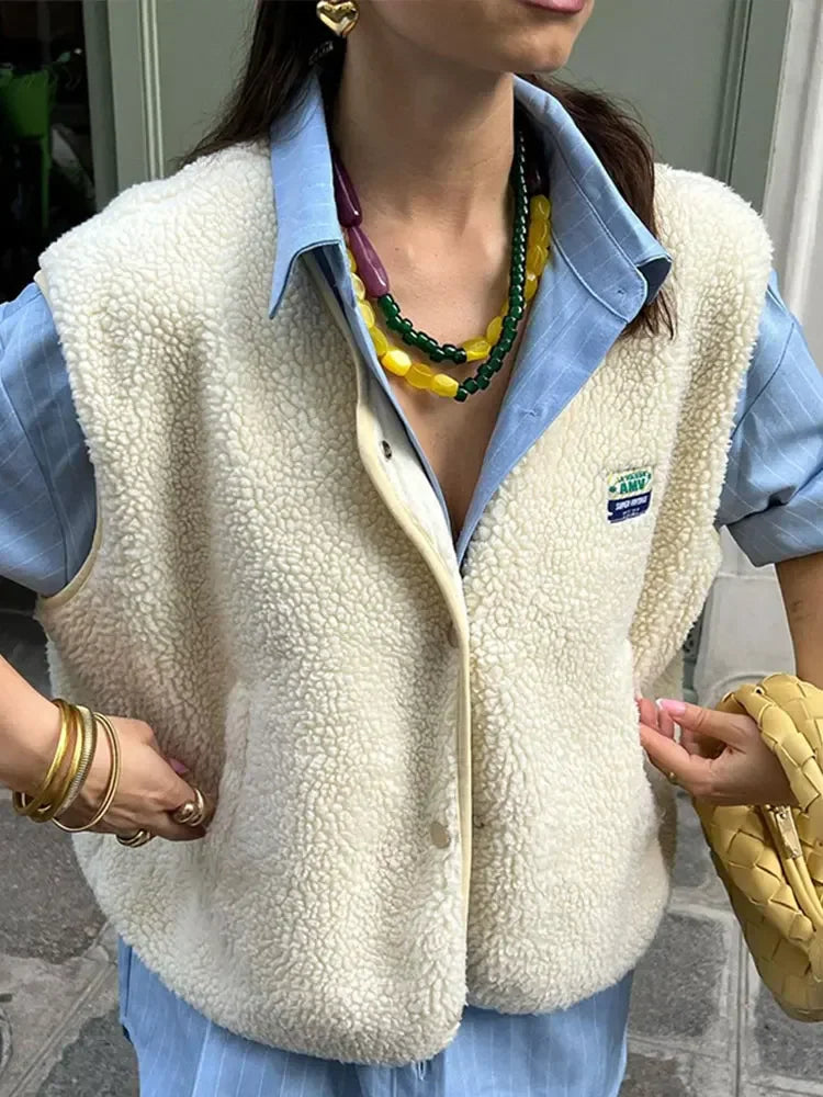 Frau trägt weiße Fleeceweste über blauem Hemd, kombiniert mit bunten Halsketten und goldenen Armreifen. Modetrend, Herbstmode, Streetstyle.