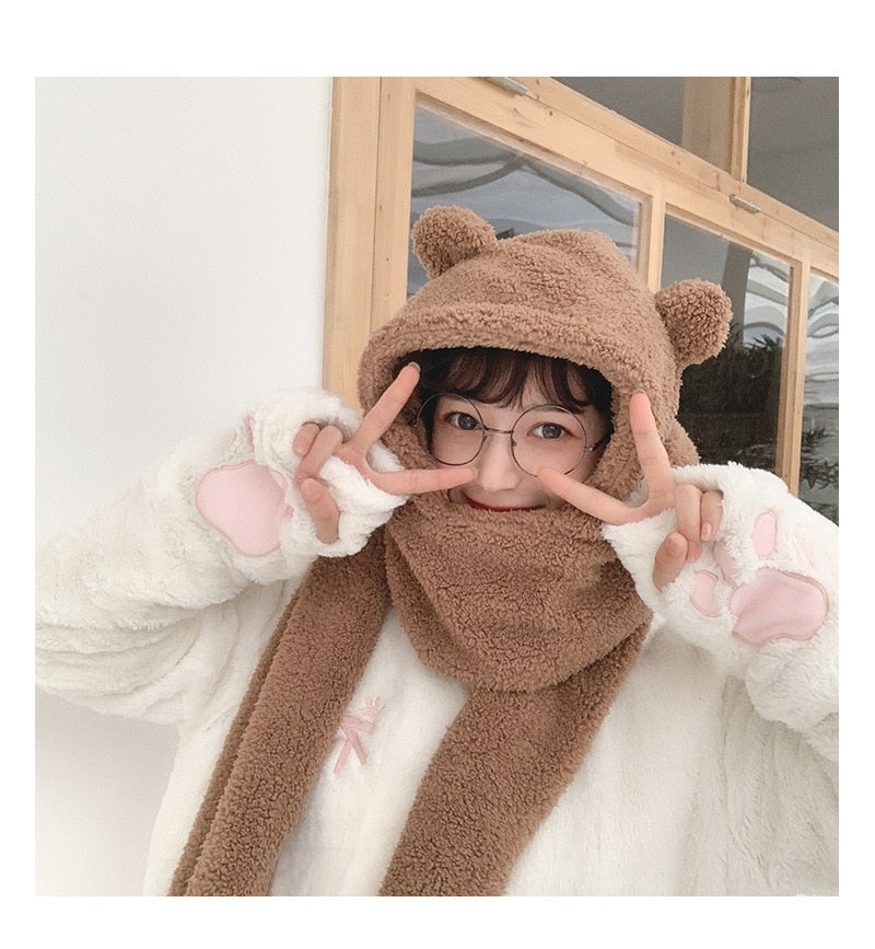 Niedliches Mädchen in Bärenmütze und Schal, trägt flauschige Handschuhe mit Pfotenmuster. Wintermode, kawaii Stil, warme Accessoires.