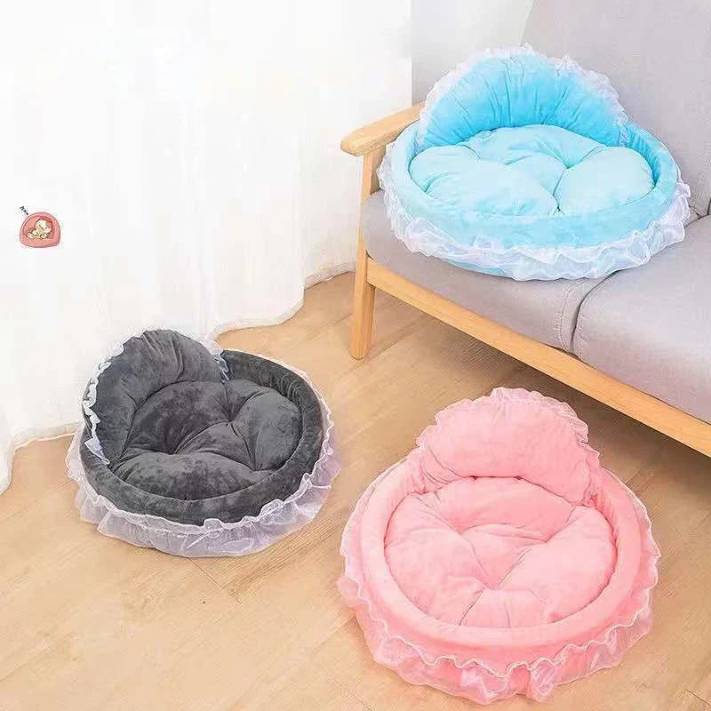 Herzförmige Haustierbetten in Blau, Grau und Rosa mit Rüschen, auf Holzboden neben Sofa.