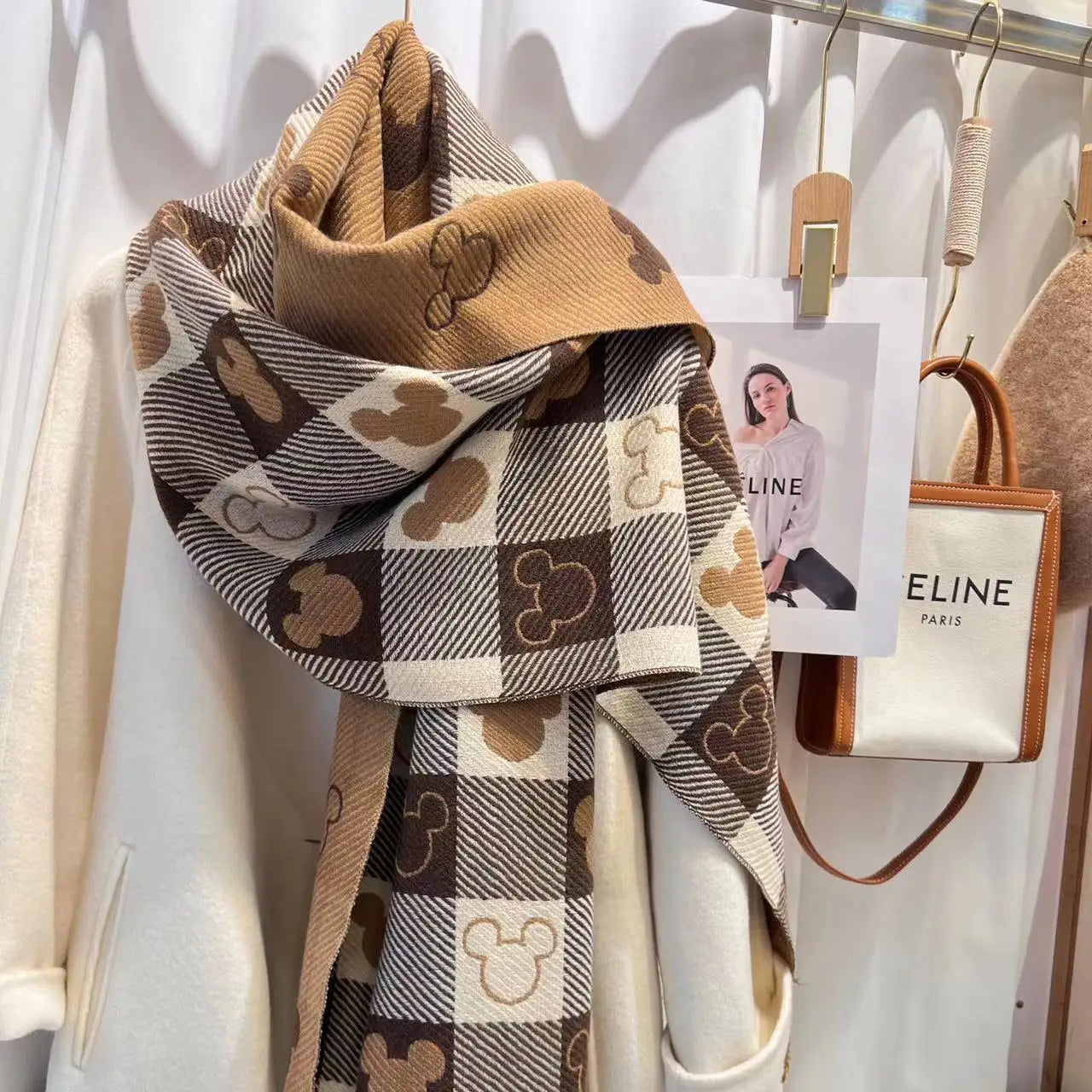 Brauner kariert gestrickter Schal mit Mickey-Maus-Motiven, drapiert über einem weißen Mantel. Modisches Accessoire, ideal für Herbst und Winter.