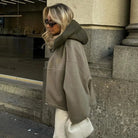 Frau in übergroßem, grauem Hoodie mit Kapuze, Sonnenbrille und weißer Tasche. Streetwear, urbaner Stil, modisch, lässig, Herbstmode.