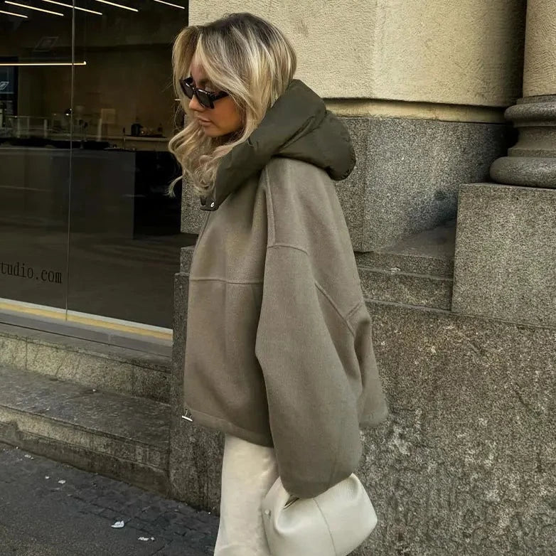 Frau in übergroßem, grauem Hoodie mit Kapuze, Sonnenbrille und weißer Tasche. Streetwear, urbaner Stil, modisch, lässig, Herbstmode.