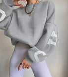 Grauer Oversize-Pullover mit Kettenhalskette und weißen Leggings. Modetrend, lässiger Stil, bequeme Kleidung, Streetwear-Look.