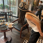 Frau mit gehäkeltem Hut in modernem Café, leere Teller auf Tisch, stilvolle Inneneinrichtung, Freizeitmode, urbaner Lifestyle.