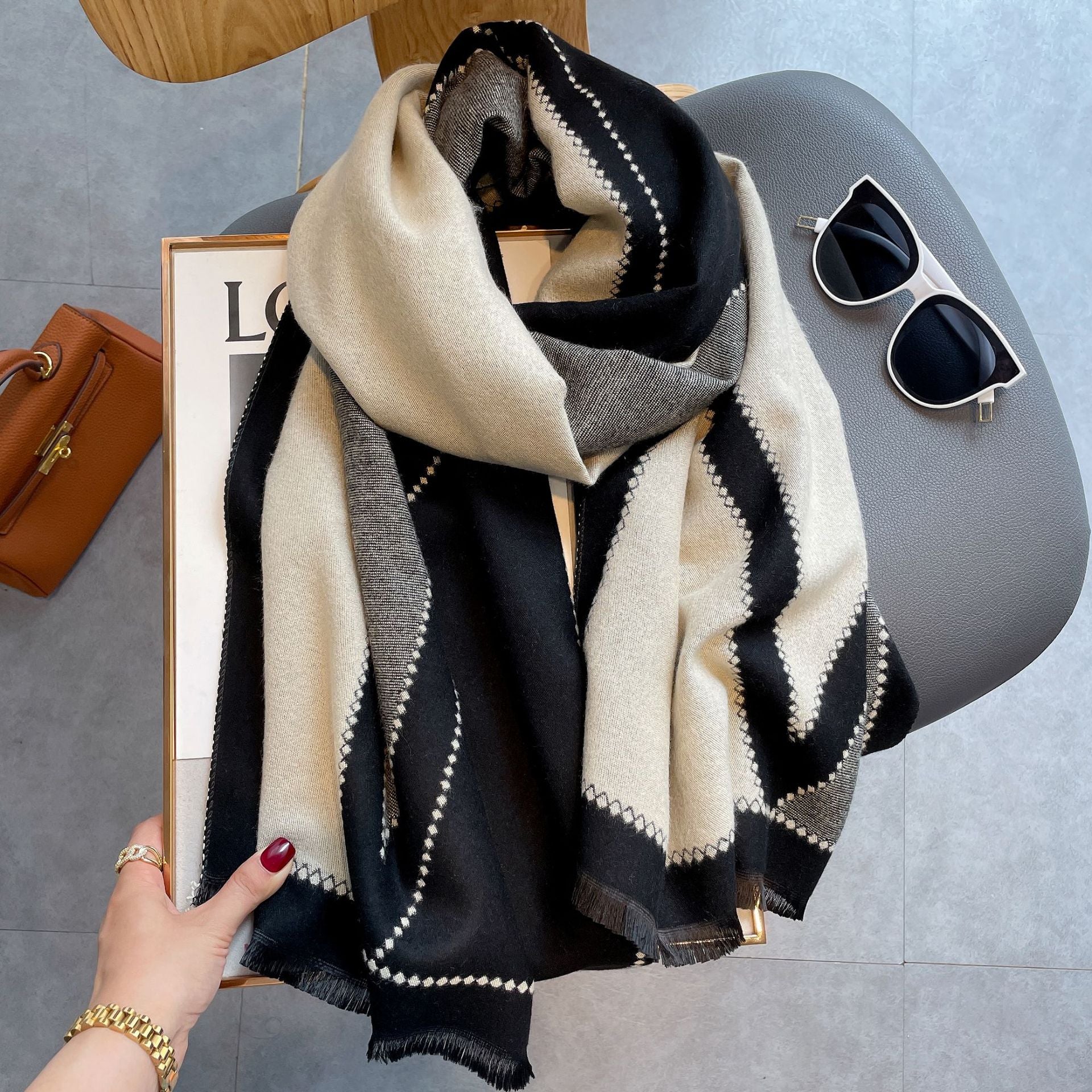 Eleganter schwarz-weißer Schal mit geometrischem Muster, ideal für Herbstmode. Perfekt kombiniert mit Sonnenbrille und brauner Handtasche.