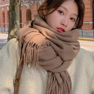 Frau mit braunem Schal und beigem Mantel vor Backsteingebäude. Herbstmode, stilvoller Look, warme Accessoires, modische Damenbekleidung.