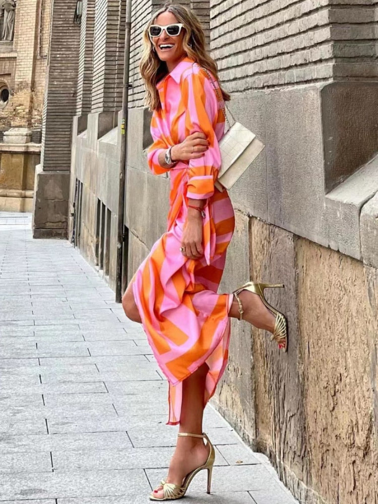 Frau in farbenfrohem, geometrisch gemustertem Kleid, posiert fröhlich auf der Straße. Modetrend, Sommerkleid, Streetstyle, Damenmode.