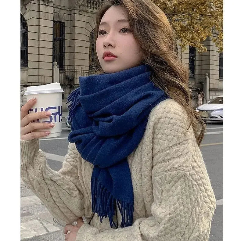 Frau in beigem Strickpullover und blauem Schal hält Kaffeebecher. Herbstmode, Streetstyle, gemütlicher Look, urbaner Hintergrund.