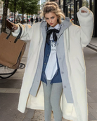 Eleganter Winterlook: Frau in weißem Oversize-Mantel, grauem Hoodie und Leggings. Trendige Mode, Streetstyle, urbane Eleganz, Herbst/Winter.