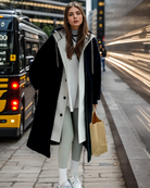 Junge Frau in modischem Wintermantel, hält Einkaufstasche. Trendige Straßenmode, urbane Kulisse, stilvolle Winterbekleidung, City-Look.