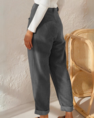 Frau in grauer Cordhose, weißem Pullover, neben Rattan-Stuhl, modisch, lässig, Herbstmode.