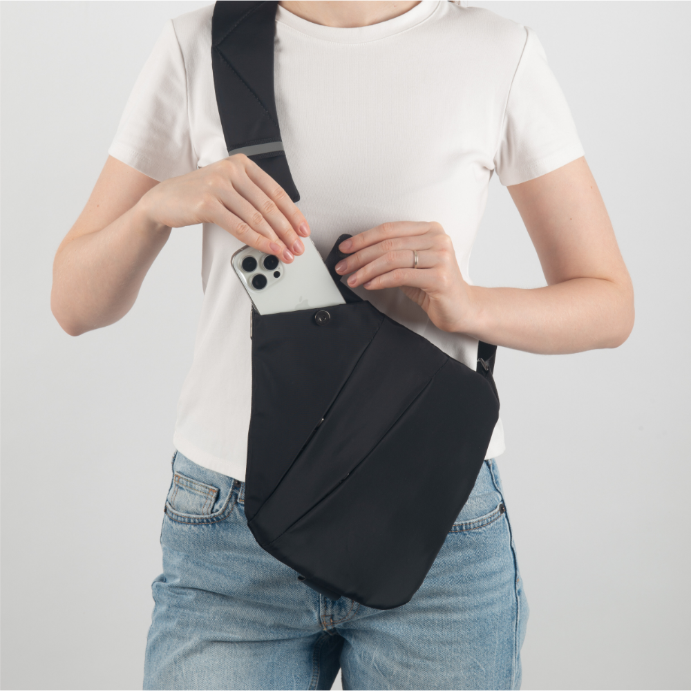 Frau mit schwarzer Umhängetasche, Smartphone, weißes T-Shirt, blaue Jeans, modisches Accessoire.