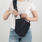 Frau mit schwarzer Umhängetasche, Smartphone, weißes T-Shirt, blaue Jeans, modisches Accessoire.