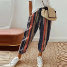Frau in gestreiften Vintage-Harajuku-Hosen, weißem T-Shirt, Strohtasche, weißen Sneakers.