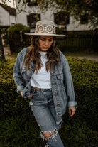 Frau in zerrissener Jeans und Jeansjacke, trägt weißen Hut mit Blumenmuster. Modetrend, lässiger Stil, Outdoor-Fotografie, Streetwear.