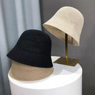 Zwei gehäkelte Sommer-Bucket-Hüte, schwarz und beige, auf einem Tisch und Ständer. Atmungsaktiv, faltbar, ideal für Strand und Outdoor.
