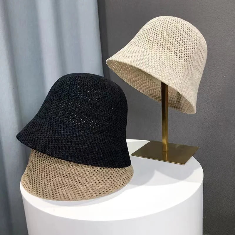 Zwei gehäkelte Sommer-Bucket-Hüte, schwarz und beige, auf einem Tisch und Ständer. Atmungsaktiv, faltbar, ideal für Strand und Outdoor.