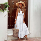 Frau in weißem Sommerkleid mit Strohhut und Korbtasche vor Holztür. Perfekter Look für Strandmode und Sommeroutfits.