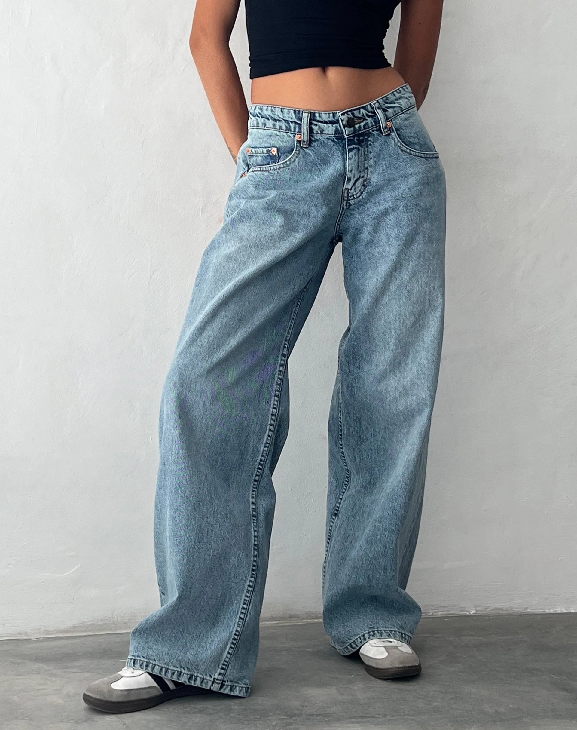 Frau trägt schwarze Lycra-Top und weite, vintage-blaue Jeans, modisch, lässig, urbaner Stil.