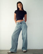 Frau in schwarzem Lycra-Top und weiten, vintage-blauen Jeans vor weißem Hintergrund.