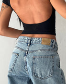 Frau in schwarzem Lycra-Top und blauen Vintage-Jeans mit weitem Schnitt, Rückansicht.