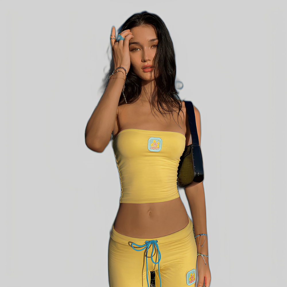 Frau in gelbem Outfit mit Tube-Top und Hose, modisch und sommerlich, vor grauem Hintergrund. Trendige Damenmode, Freizeitkleidung, Streetstyle.