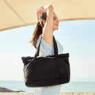 Frau mit schwarzer Tragetasche, Sommerkleid, Strandhintergrund, Modeaccessoire, Freizeitlook.