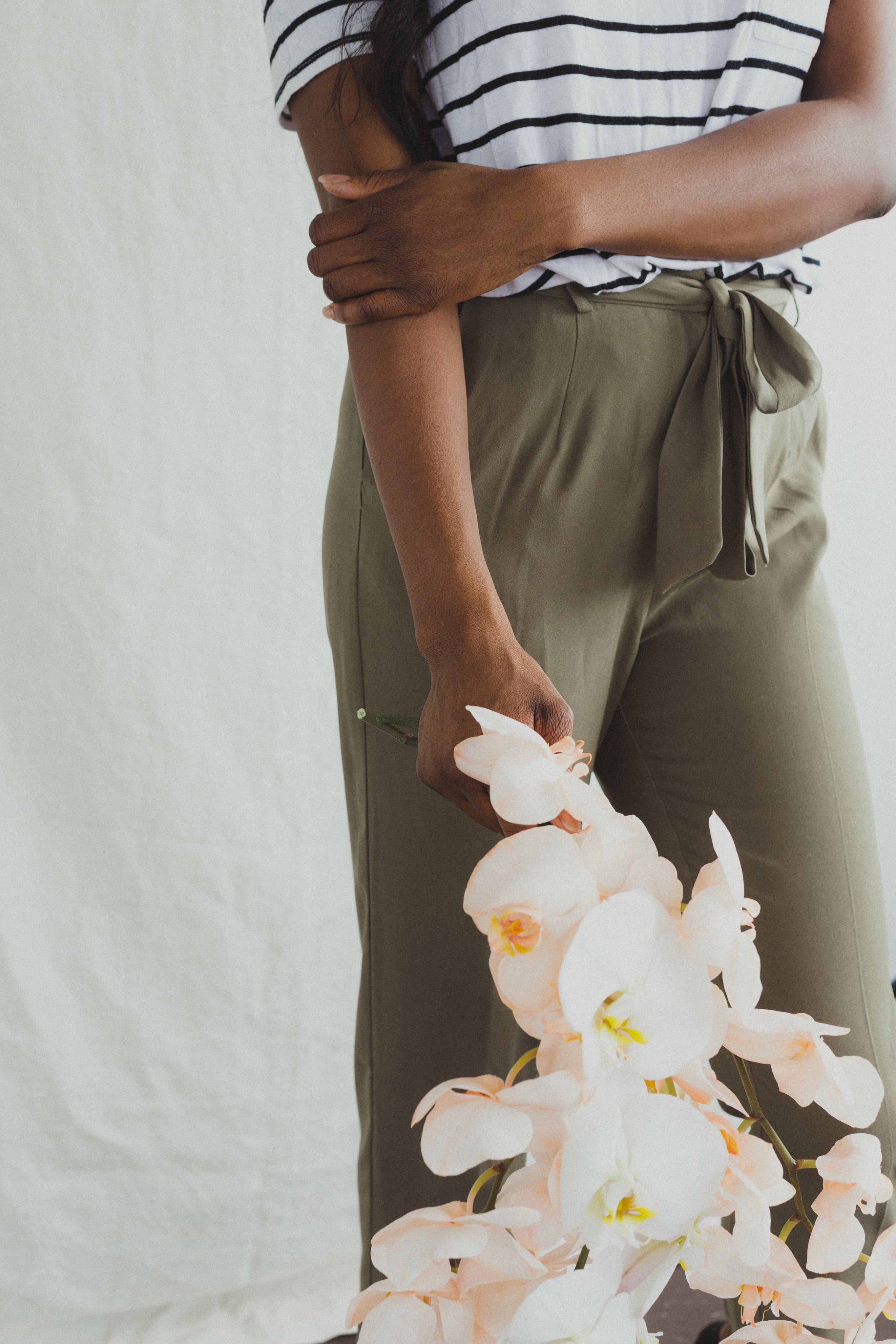 Frau in gestreiftem Shirt und khakifarbenen Hosen hält weiße Orchideen. Mode, Blumen, Stil, Eleganz, Sommeroutfit, Orchideenstrauß.