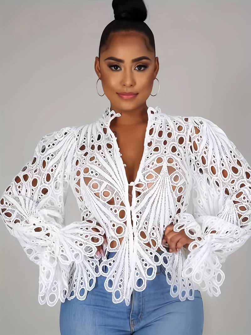 Frau trägt weiße Spitzenbluse mit auffälligem Lochmuster, kombiniert mit blauen Jeans. Modetrend, elegante Damenmode, stilvolle Oberbekleidung.