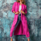 Frau in pinkem Strickmantel mit Noppen, kombiniert mit weißem Top und Jeans. Modetrend, Strickmode, Damenbekleidung, stilvoll, modern.