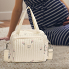 Weiße Wickeltasche mit Blumenmuster, gesteppt, vor schwangerer Frau auf Teppich.