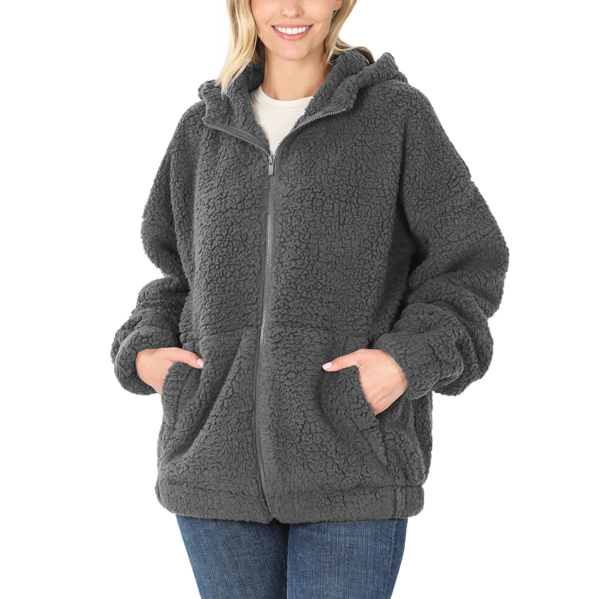Frau in grauer Fleecejacke mit Kapuze, Reißverschluss und Taschen, lässiger Winterstil.