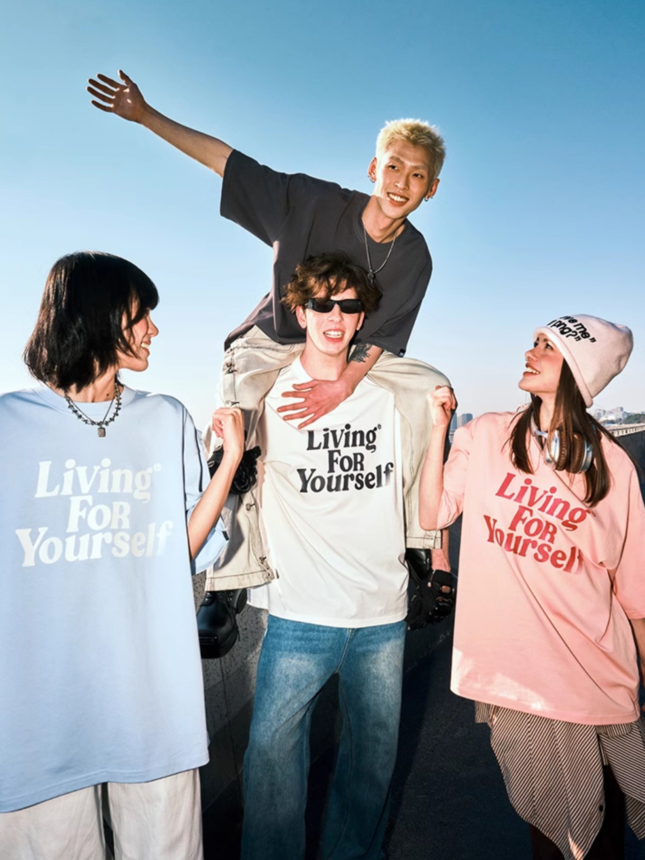Vier junge Erwachsene in modischen T-Shirts mit dem Slogan "Living for Yourself" posieren fröhlich im Freien. Streetwear, Freundschaft, Lifestyle.
