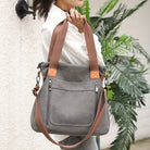 Graue Canvas-Tasche mit braunen Ledergriffen, Reißverschlusstaschen und verstellbarem Schultergurt. Stilvoll, praktisch, ideal für den Alltag.