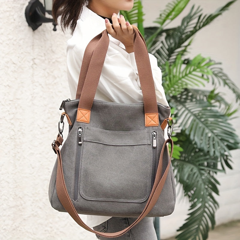 Graue Canvas-Tasche mit braunen Ledergriffen, Reißverschlusstaschen und verstellbarem Schultergurt. Stilvoll, praktisch, ideal für den Alltag.