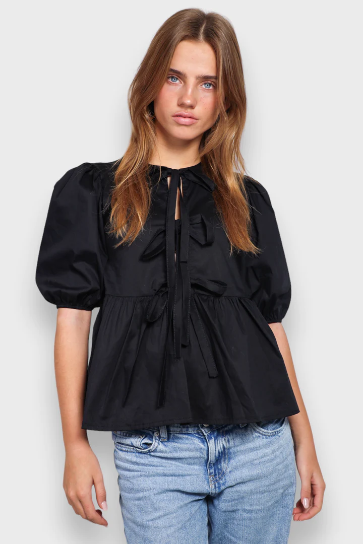 Schwarze Damenbluse mit Puffärmeln und Schleifen, kombiniert mit blauen Jeans. Modetrend, stilvolle Oberbekleidung, lässiger Look.