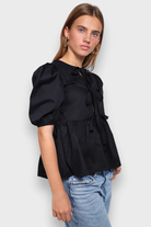 Schwarze Damenbluse mit Puffärmeln und Schleifendetails, kombiniert mit blauen Jeans. Modetrend, stilvolle Oberbekleidung, elegantes Design.