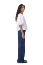 Frau in weißer Bluse und blauer Jeans mit weitem Schnitt, seitlich stehend. Modetrend, Damenbekleidung, lässiger Stil, Streetwear.