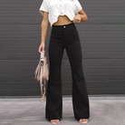 Frau in schwarzer Schlaghose und weißem Crop-Top vor grauer Wand, hält beige Handtasche. Modetrend, Damenbekleidung, Streetstyle.