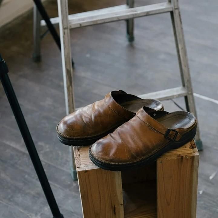 Braune Lederschuhe auf Holzblock vor Leiter, rustikaler Stil, handgefertigte Clogs, Vintage-Design, ideal für Mode- und Schuhliebhaber.