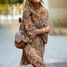 Frau in geblümtem Kleid mit langen Ärmeln, braune Umhängetasche, lächelnd, modisch, urbaner Hintergrund, Herbstmode, stilvoll, elegant.