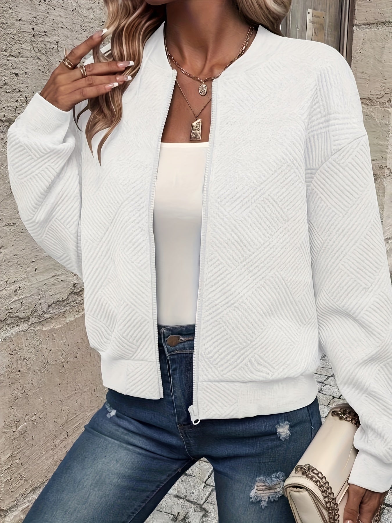 Damenmode: Weiße Bomberjacke mit geometrischem Muster, kombiniert mit Jeans und Tasche. Trendige Freizeitkleidung für stilvolle Outfits.