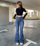 Frau in hoch taillierter, ausgestellter Stretch-Jeans und schwarzem Top. Modetrend, bequeme Passform, urbaner Stil, Denim-Look.