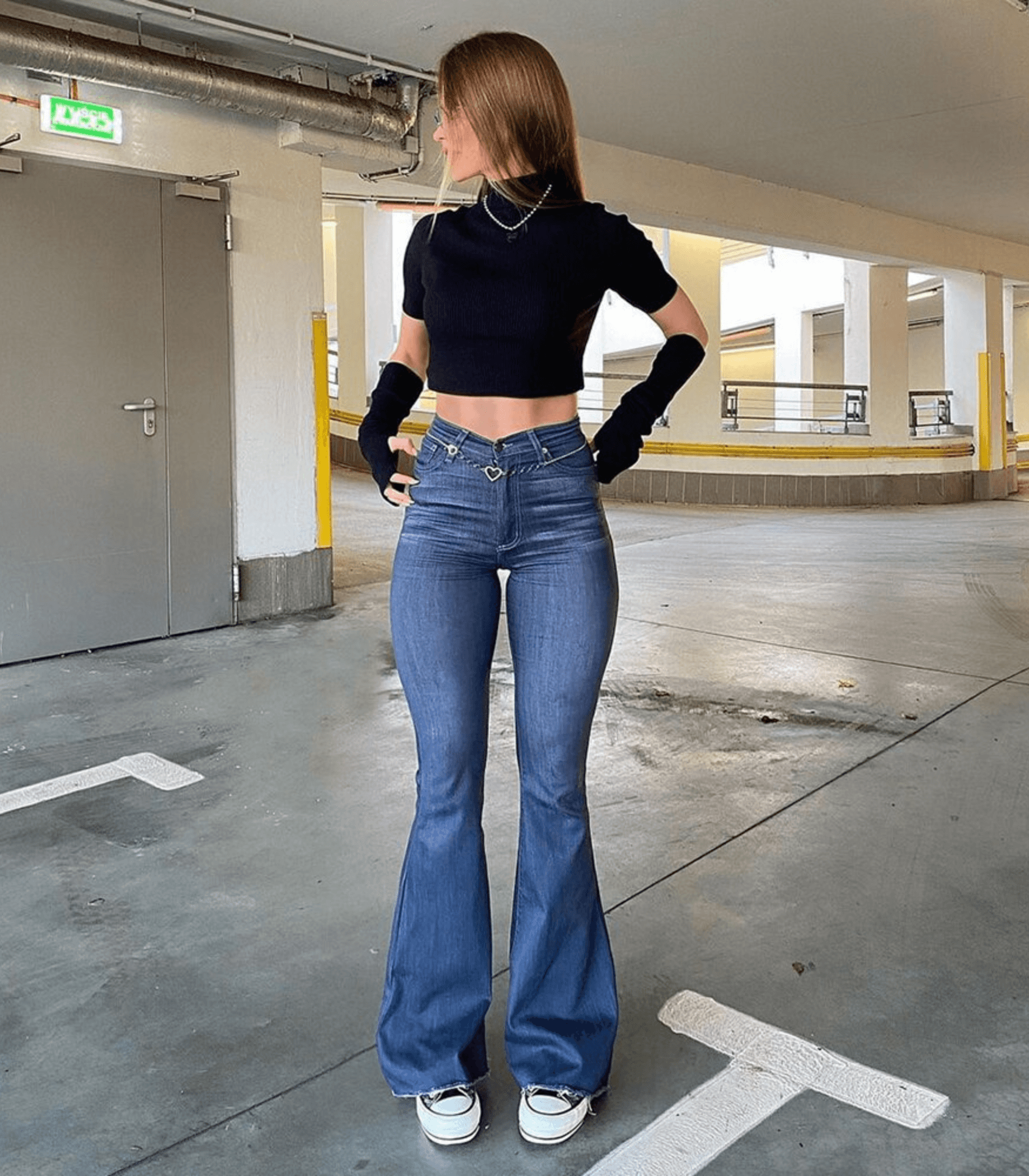 Frau in hoch taillierter, ausgestellter Stretch-Jeans und schwarzem Top. Modetrend, bequeme Passform, urbaner Stil, Denim-Look.