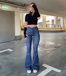 Frau in hoch taillierter, ausgestellter Stretch-Jeans, kombiniert mit schwarzem Crop-Top und Sneakers. Modetrend, bequeme Passform, urbaner Stil.