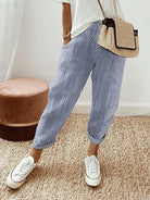 Gestreifte, blaue Leinenhose für Damen, kombiniert mit weißen Sneakers und einer beigen Umhängetasche. Perfekt für lässige Sommermode.