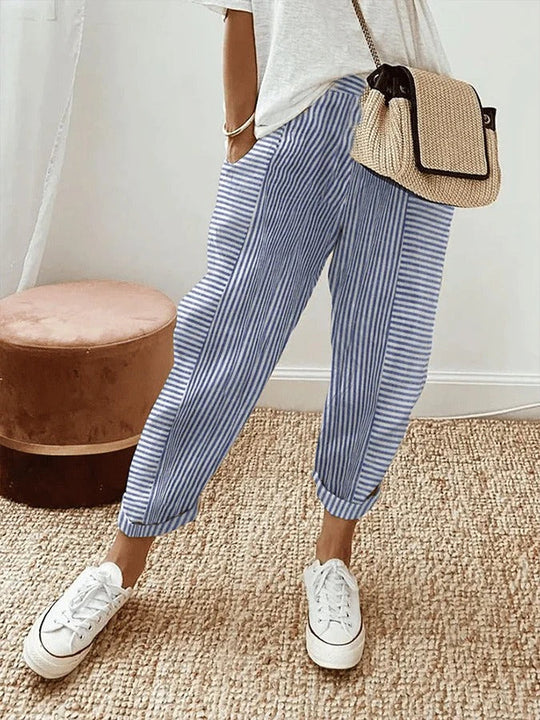 Gestreifte, blaue Leinenhose für Damen, kombiniert mit weißen Sneakers und einer beigen Umhängetasche. Perfekt für lässige Sommermode.