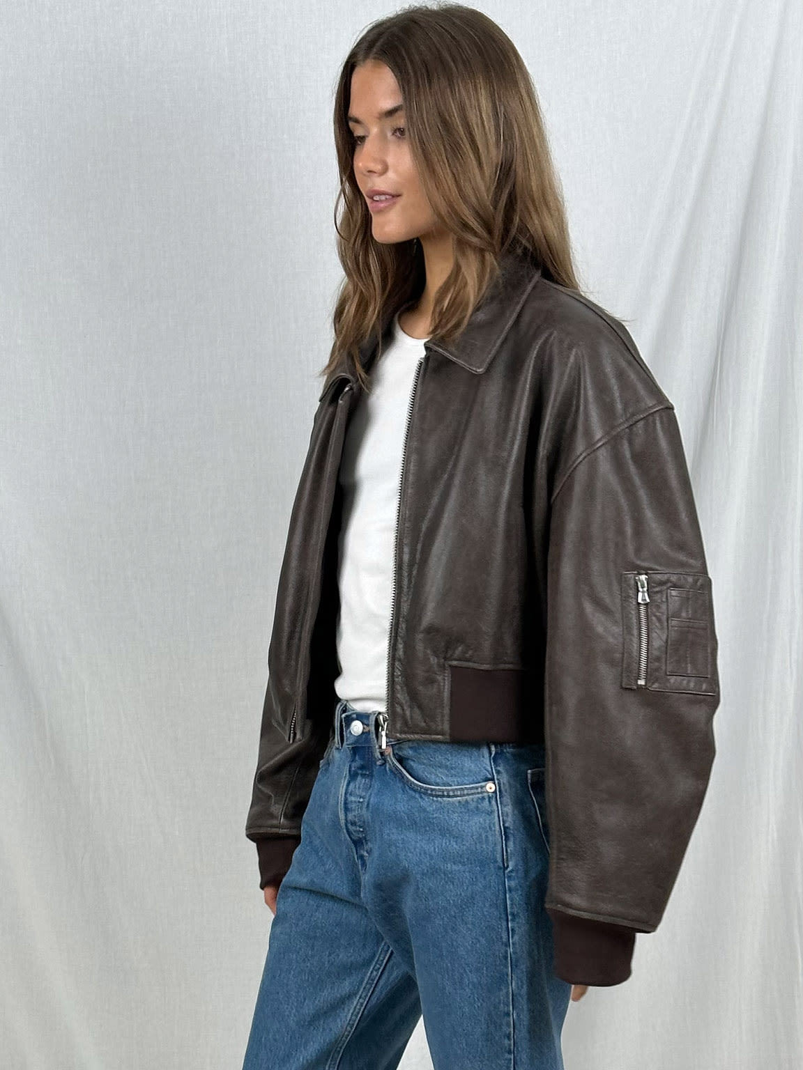 Frau in brauner Lederjacke, weißem T-Shirt und blauer Jeans. Modetrend, lässiger Look, Damenmode, Herbstoutfit, stilvolle Jacke.